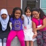 Four students sit together on a playground and smile for a photo